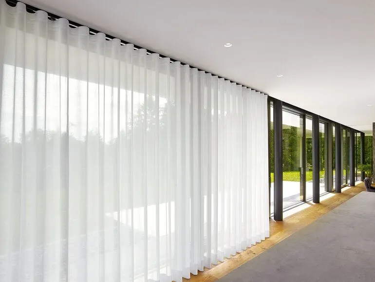 Weiße transparente Wellenband-Gardine vor einer bodentiefen Fensterfront mit Blick in den Garten